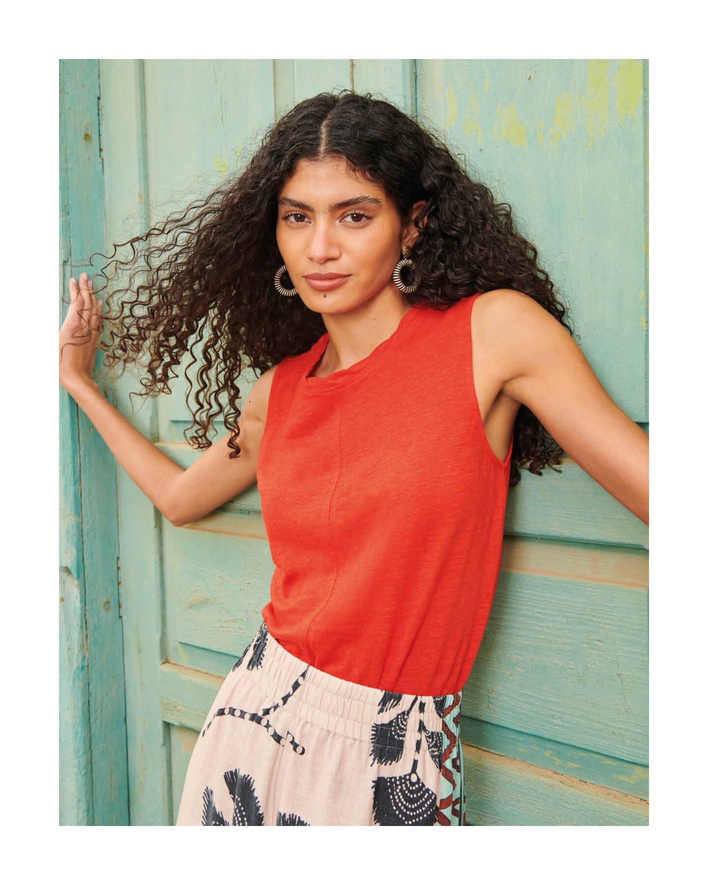 woman wearing red linen top leaning onto wooden door